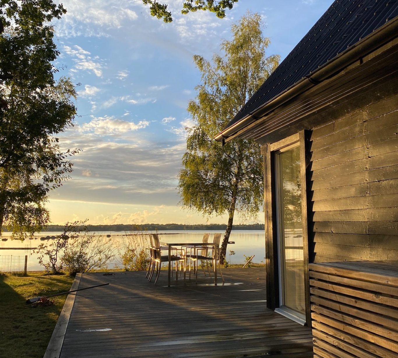 Blick auf Idyllische Seelandschaft mit Holzhaus und Terrasse bei farbigem Sonnenuntergang.