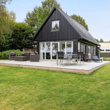 Schwarzes Holzhaus mit Terrasse, umgeben von Rasen und Bäumen.