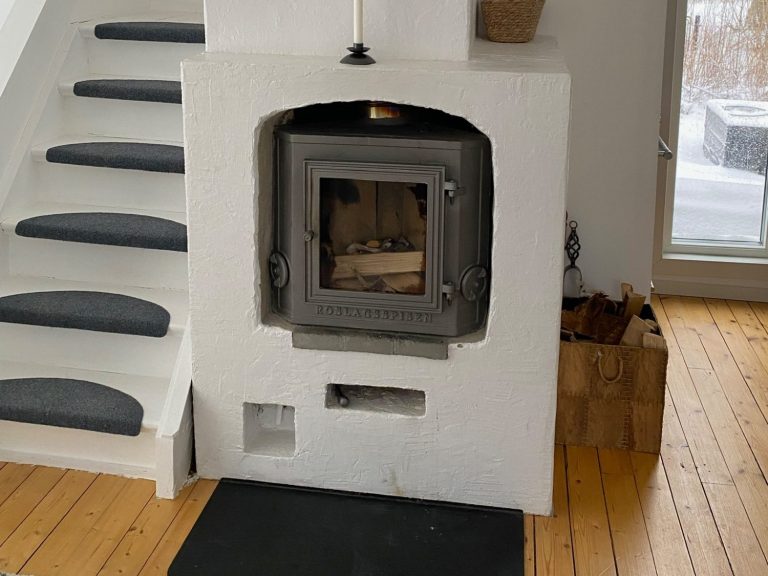 Schwedischer Kamin in einem hellen Raum mit Holzfußboden und Treppe nach oben.