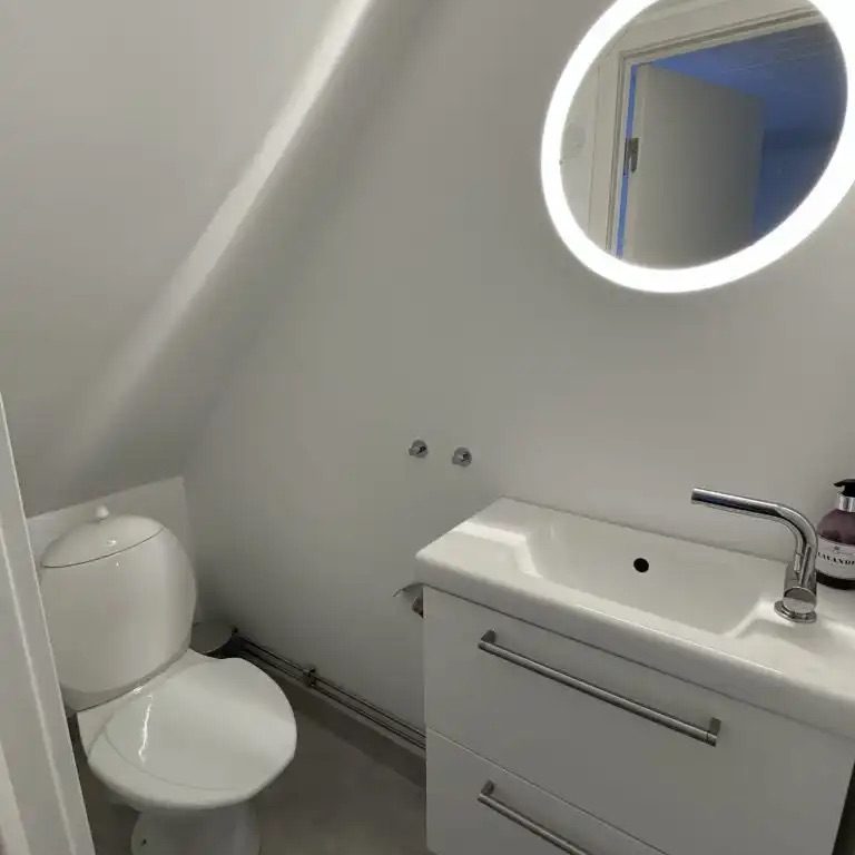 Kleines, modernes Badezimmer mit Toilette, Waschbecken und runder Spiegelleuchte.