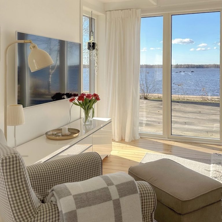 Heller Wohnbereich mit grauem Sofa, Tisch und Blick auf einen verschneiten See.