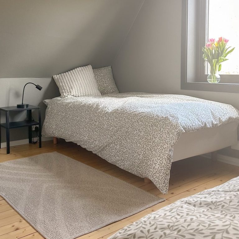 Helles, schlichtes Schlafzimmer mit zwei Betten, Stuhl und Fenster mit Blick nach draußen.