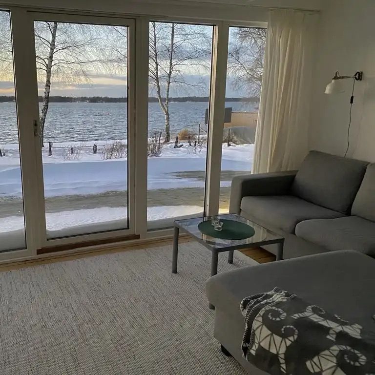 Heller Wohnbereich mit grauem Sofa, Tisch und Blick auf einen verschneiten See.