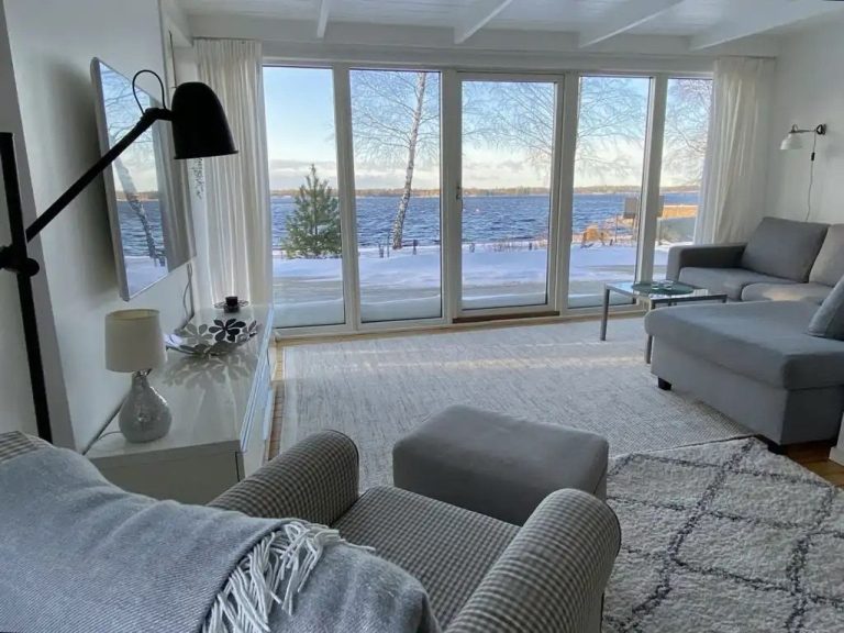 Helles Wohnzimmer mit großer Fensterfront und Blick auf den See in verschneiter Landschaft.