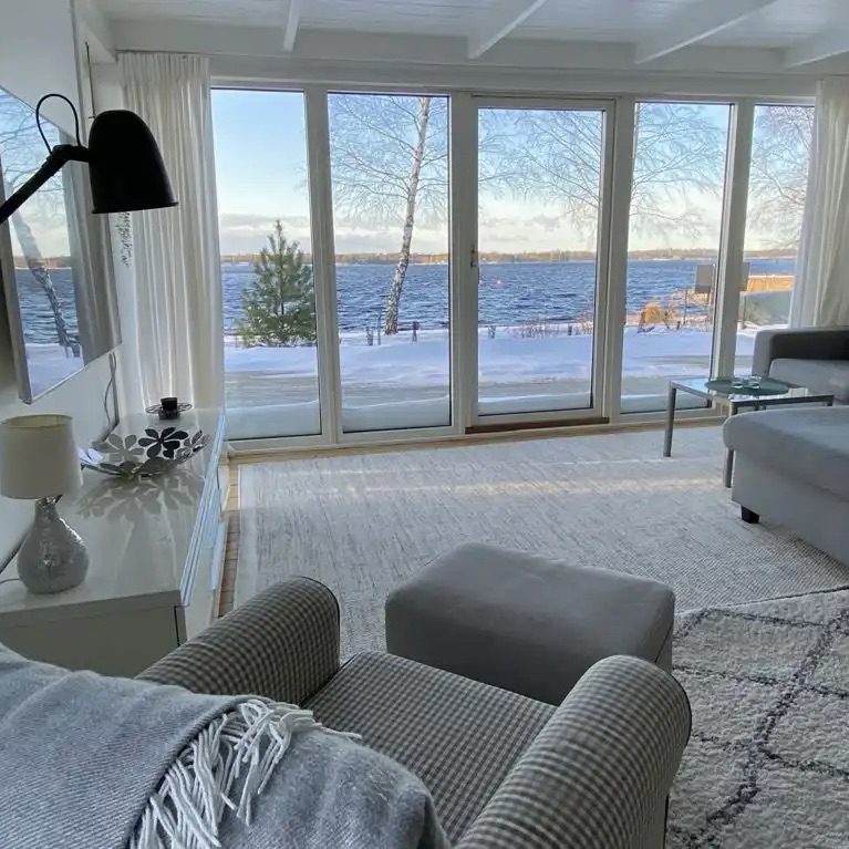 Helles Wohnzimmer mit Blick auf den Schnee und den See durch große Fensterfront.