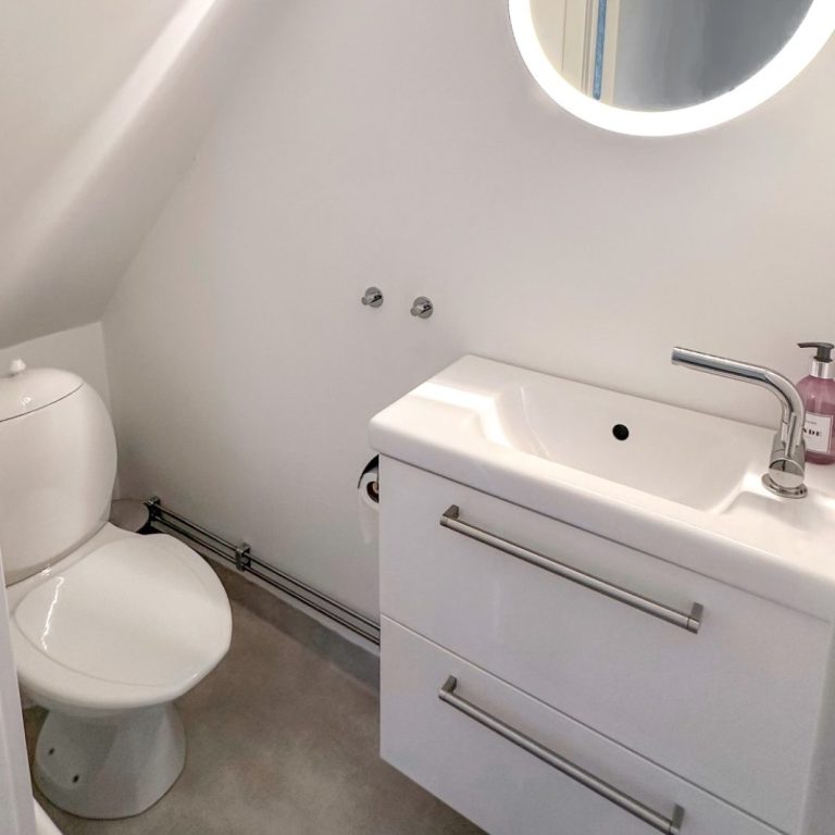 Kleines, modernes Badezimmer mit Toilette, Waschbecken und runder Spiegelleuchte.