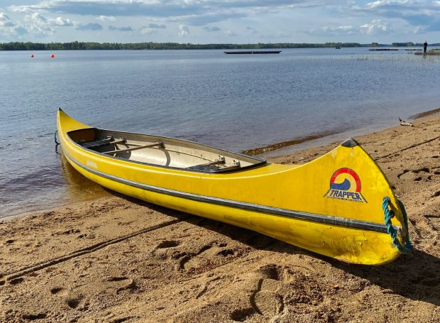 Gelbes Kanu am Ufer eines ruhigen Gewässers mit sandigem Strand im Hintergrund.