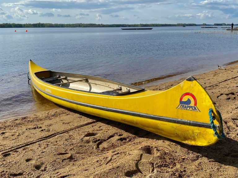 Gelbes Kanu am Ufer eines ruhigen Gewässers, umgeben von Sandstrand.