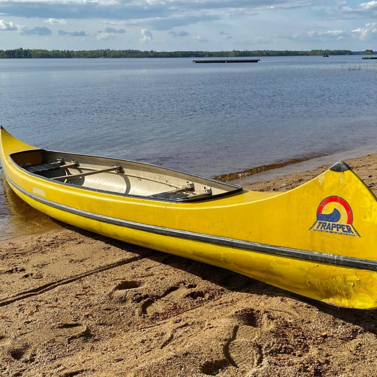 Gelbes Kanu am Ufer eines ruhigen Sees mit Sandstrand.