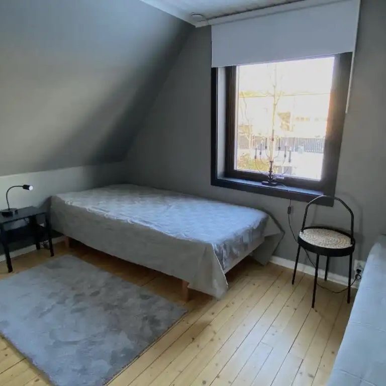 Helles, schlichtes Schlafzimmer mit zwei Betten, Stuhl und Fenster mit Blick nach draußen.