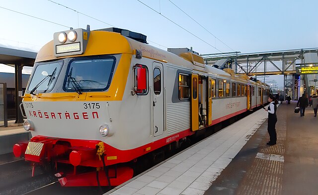 Orange und weiße Regionalbahn an einem Bahnhof, mit Reisenden auf dem Bahnsteig.